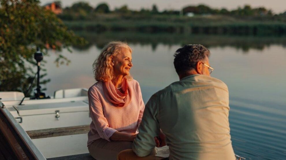 retired couple in a canoe_2624156587 A retired couple in a canoe on a placid, silver lake with trees, brush and mountains softly unfocused in the background.